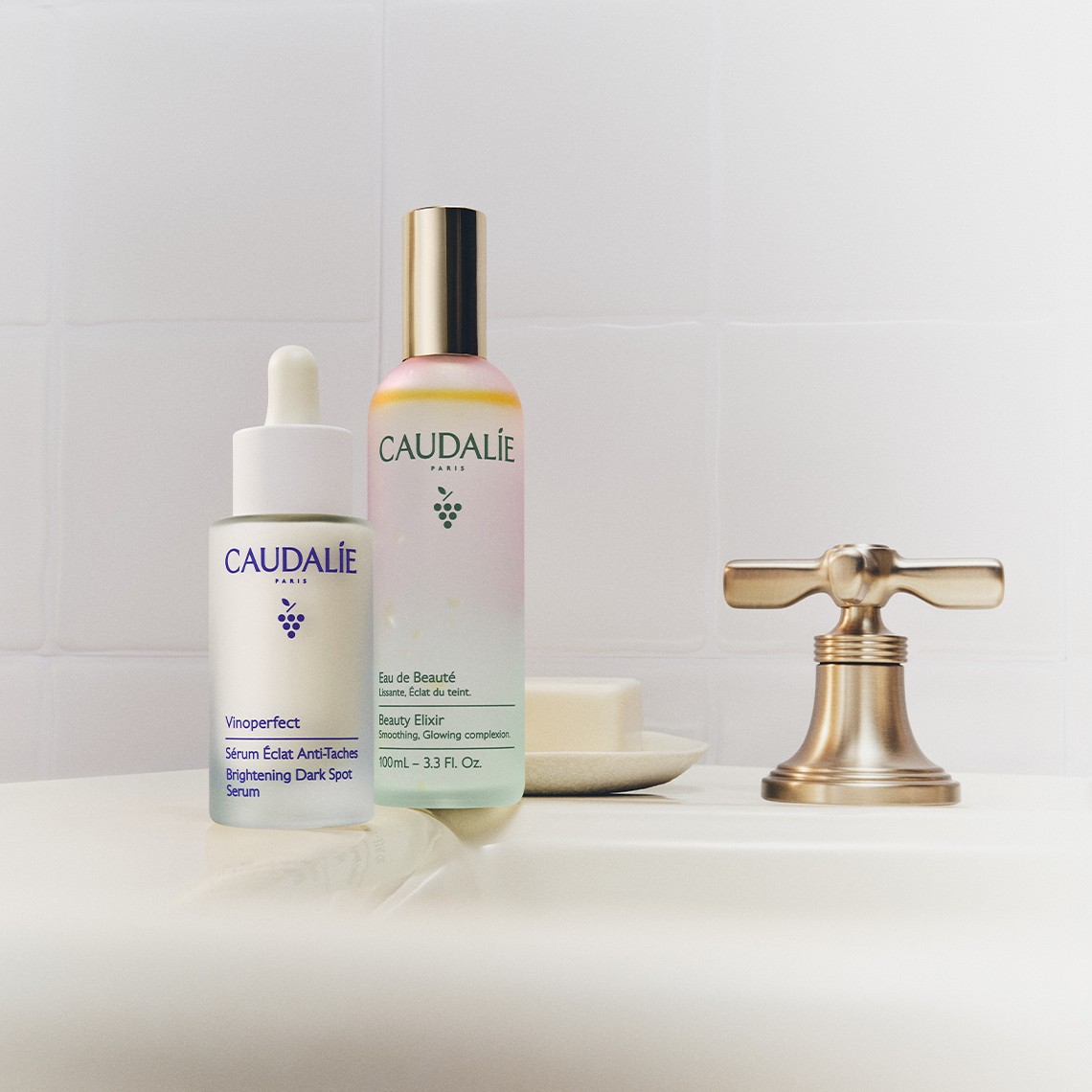 Two Caudalie skincare products on a white bathroom sink with a gold faucet. A bar of soap is placed in the background.