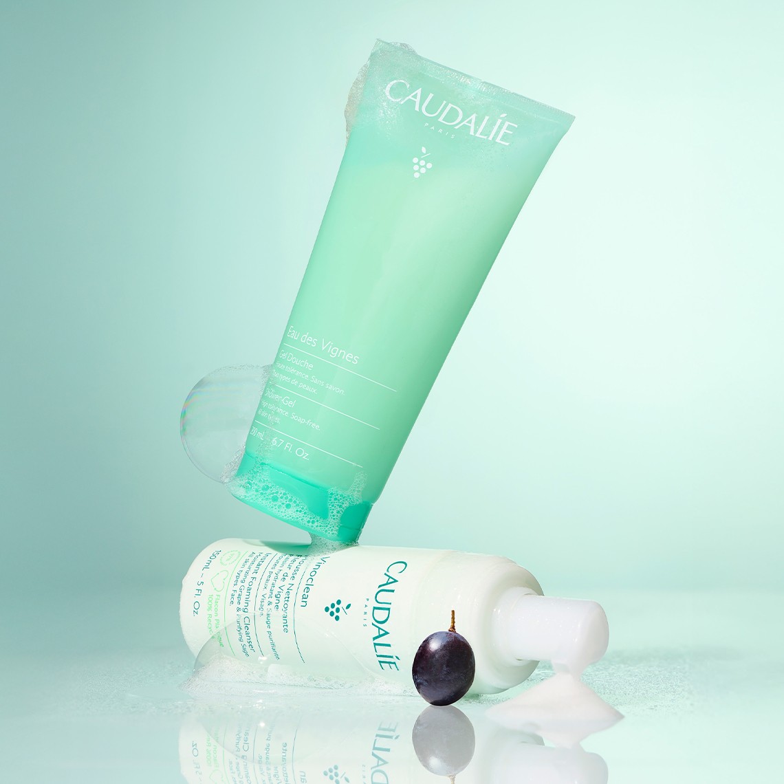 Aqua-themed skincare products, including a tube and bottle, on a reflective surface with a soft, green gradient background.