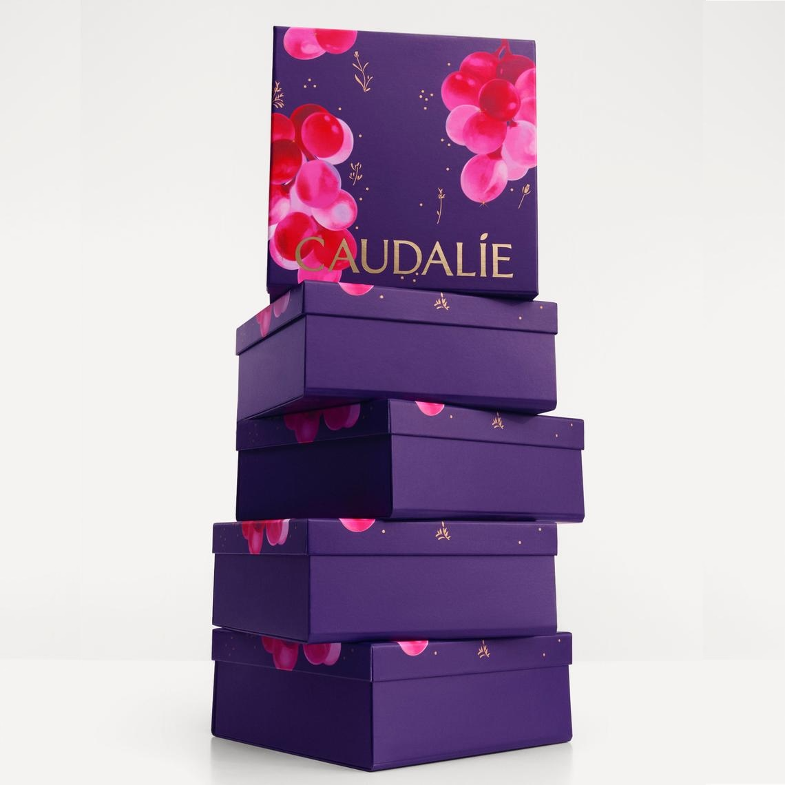 A stack of purple Caudalie gift boxes with pink grape designs against a white background.