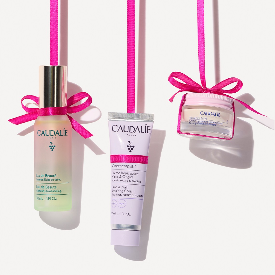 Skincare products with pink ribbons hang against a white background, symmetrically arranged on both sides.