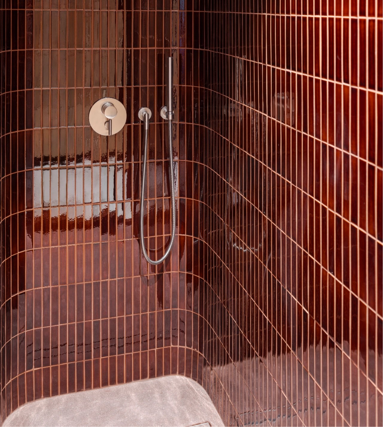 Shower area with curved brown tile walls, a minimalist round faucet, and a sleek hand-held showerhead.