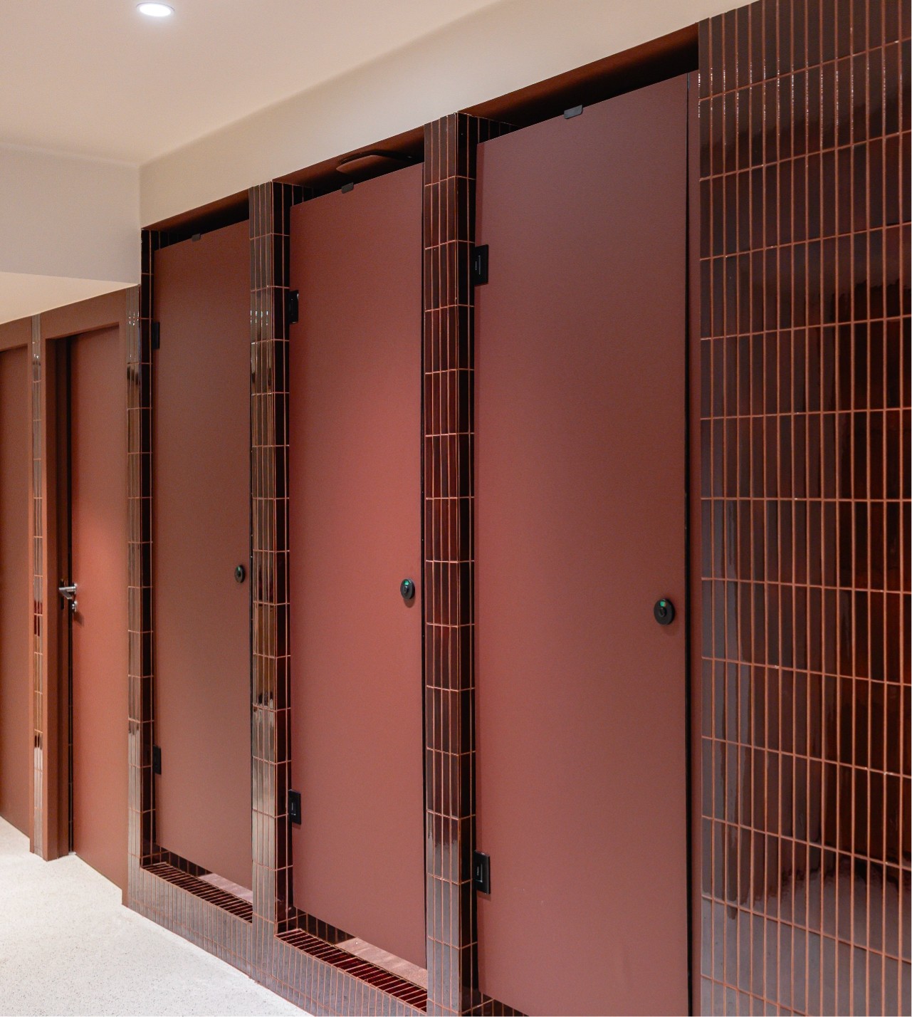A row of red restroom stalls with matching doors and brick-patterned tiles, creating a clean and modern look.