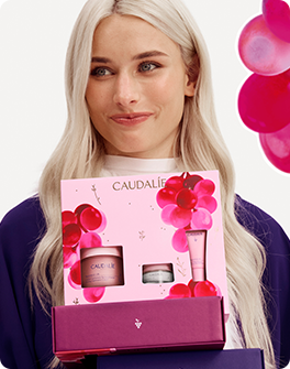 Woman holding Caudalie gift set with pink packaging and grape design, smiling.