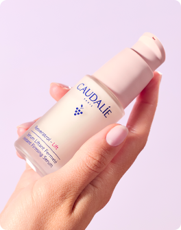 Hand holding a Caudalie beauty product bottle against a pink background, showcasing skincare cosmetics packaging.