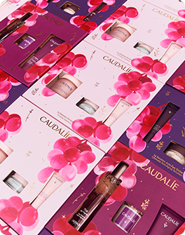 Caudalie skincare gift sets with grape illustrations on pink and purple packaging, featuring various creams and bottles.