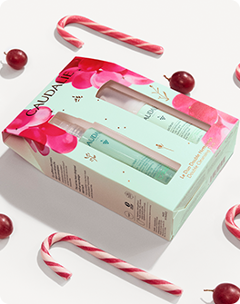 Caudalie gift set with two skincare products in a colorful box, surrounded by candy canes and red berries on a white background.