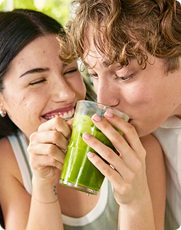 A smiling couple enjoys a glass of green juice together, sharing a moment of laughter and happiness.
