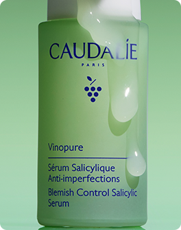 A Caudalie Vinopure salicylic serum bottle with a glossy liquid texture against a green background.