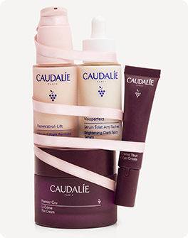 A set of Caudalie skincare products wrapped in a light pink ribbon, including serums and eye cream, with elegant packaging.