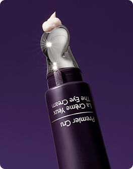 A purple eye cream tube with a silver applicator tip, dispensing a small amount of cream, against a solid purple background.