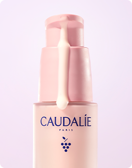 Caudalie Paris skincare serum bottle with pink pump dispenser on light lavender background.