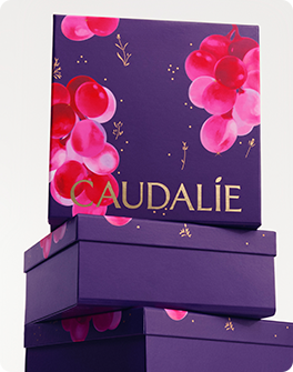 Purple gift boxes with gold "Caudalie" text and pink grape illustrations, stacked against a light background.