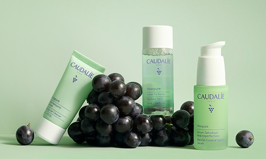 Caudalie skincare products with green packaging, displayed alongside a bunch of grapes on a light green background.