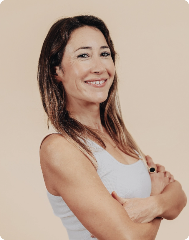 Smiling woman with long brown hair in a white top, arms crossed, against a soft beige background.