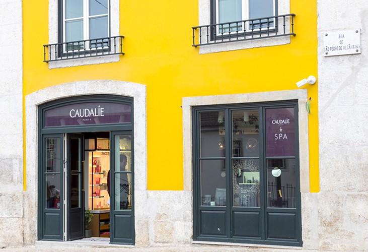 Storefront with bright yellow walls and dark green doors, displaying "Caudalie" signage. Street sign reads "Rua de São Pedro de Alcântara."