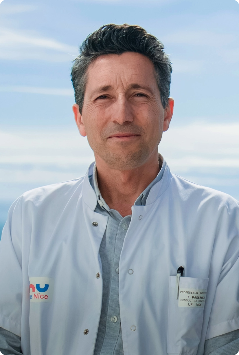 A man in a white lab coat with a badge stands outdoors against a blue sky, looking at the camera.