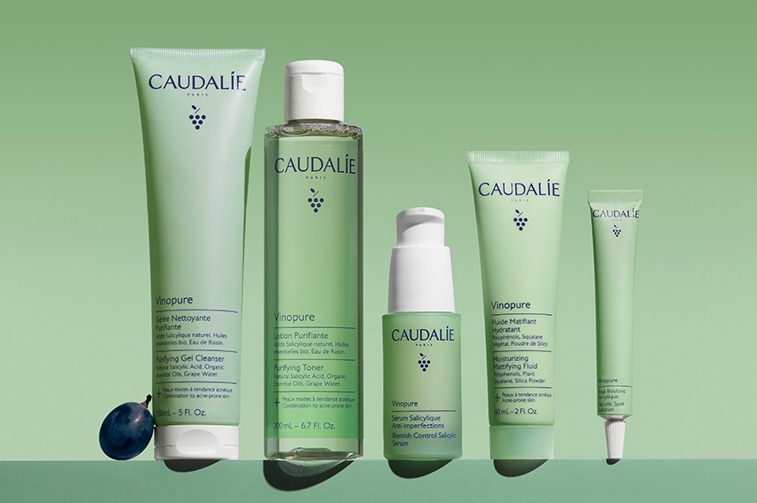 A range of Caudalie Vinopure skincare products, including cleanser, toner, serum, and moisturizer, displayed against a green background.
